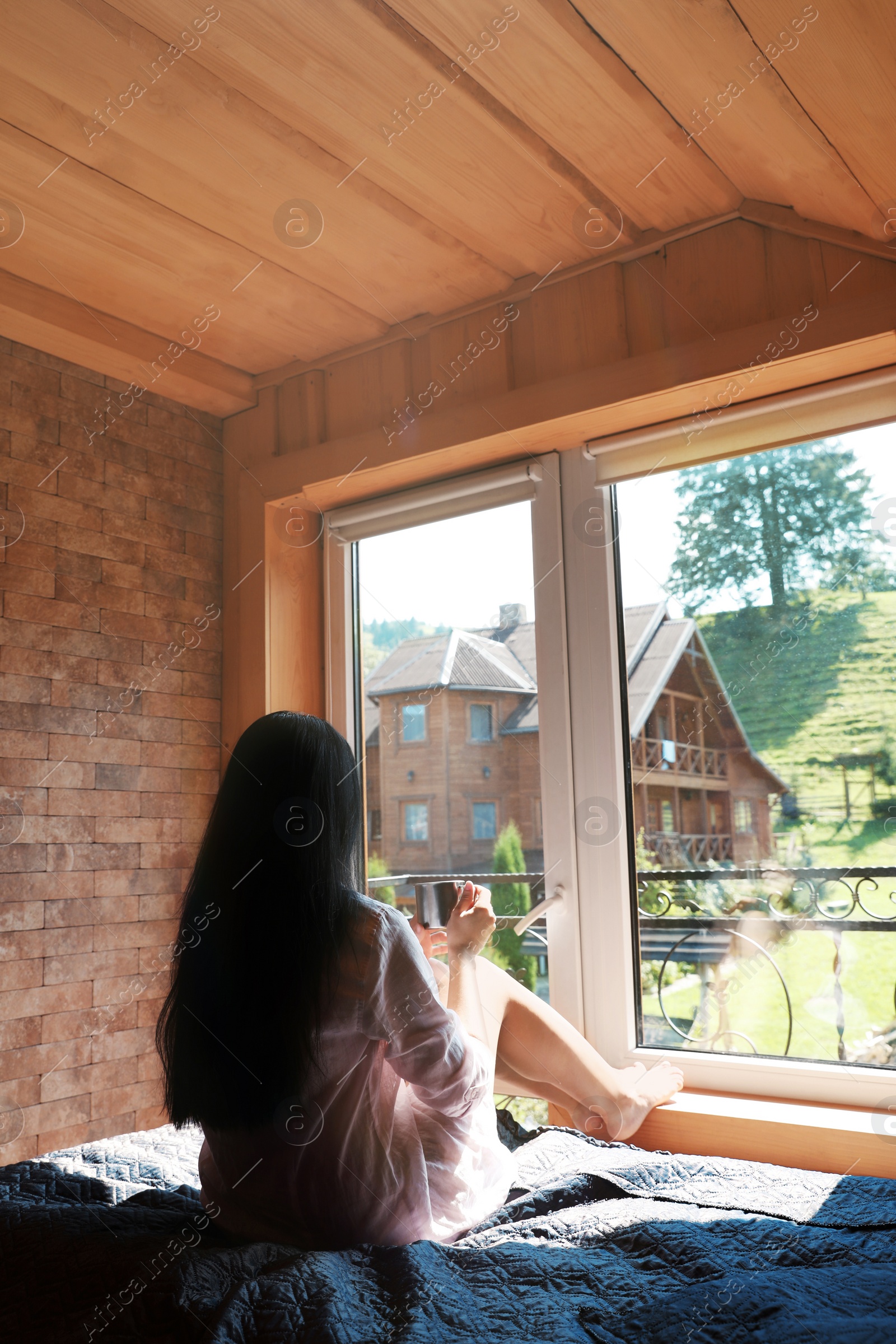 Photo of Young woman sitting on bed and enjoying view from window. Peaceful morning