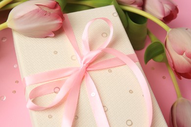 Beautiful gift box with bow, tulips and confetti on pink background, closeup