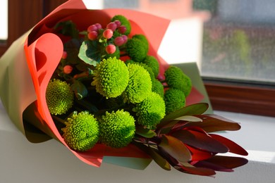 Photo of Bouquet of beautiful flowers wrapped in paper on window sill indoors, closeup