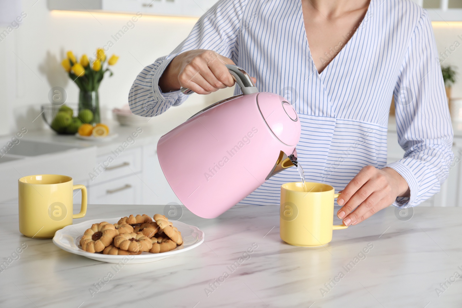 Photo of Woman pouring hot water from modern electric kettle in cup indoors, closeup