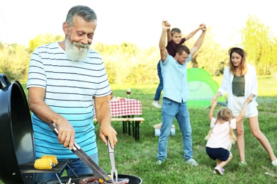 Photo of Happy senior man cooking food on barbecue grill and his family in park