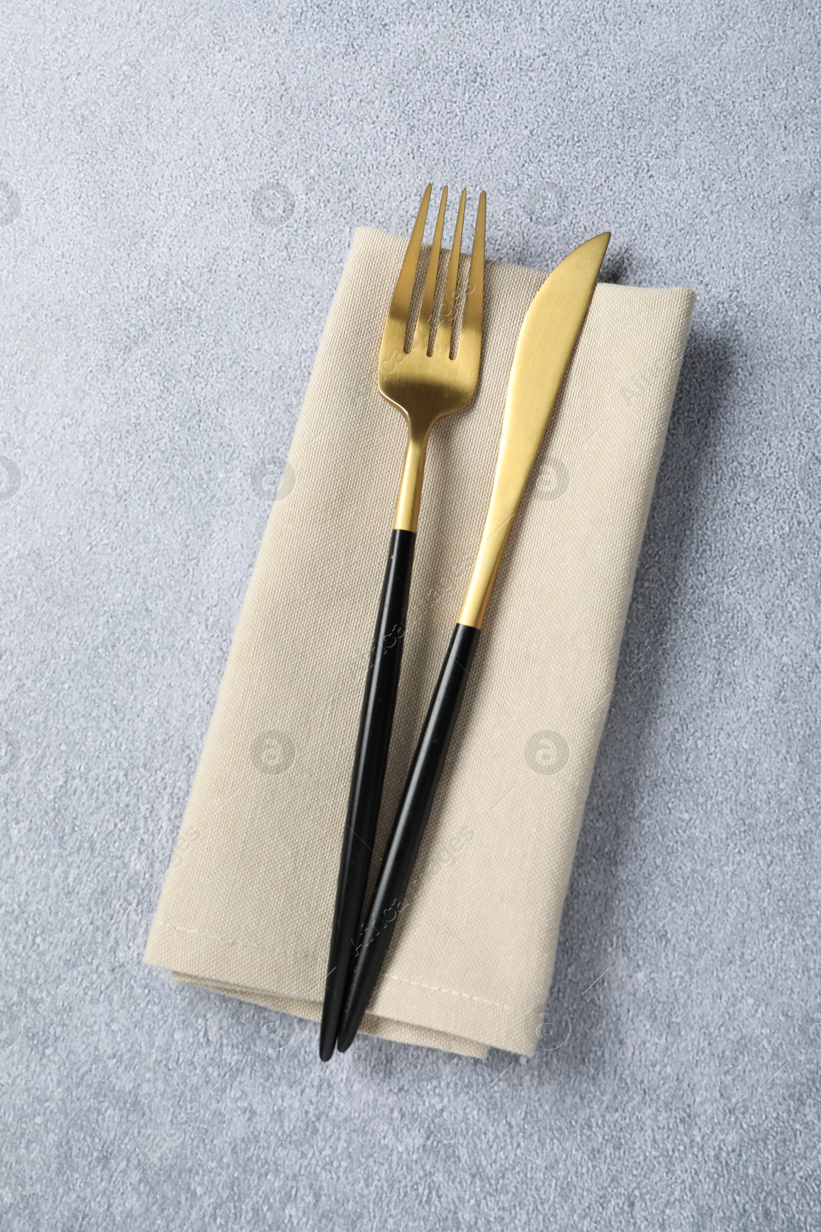 Photo of Stylish golden cutlery and napkin on grey table, top view