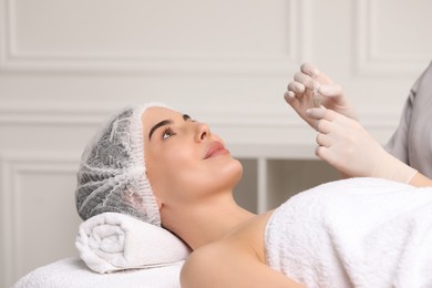 Photo of Professional cosmetologist holding skincare ampoule while working with client in clinic, closeup