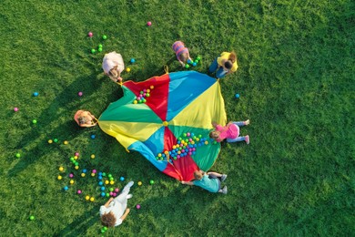 Photo of Group of children and teachers playing with rainbow playground parachute on green grass, top view. Summer camp activity