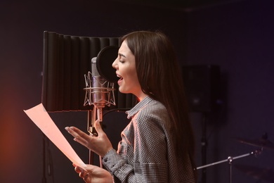 Photo of Young singer with microphone recording song in studio