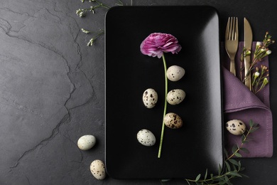 Festive Easter table setting with quail eggs and floral decoration on dark background, flat lay