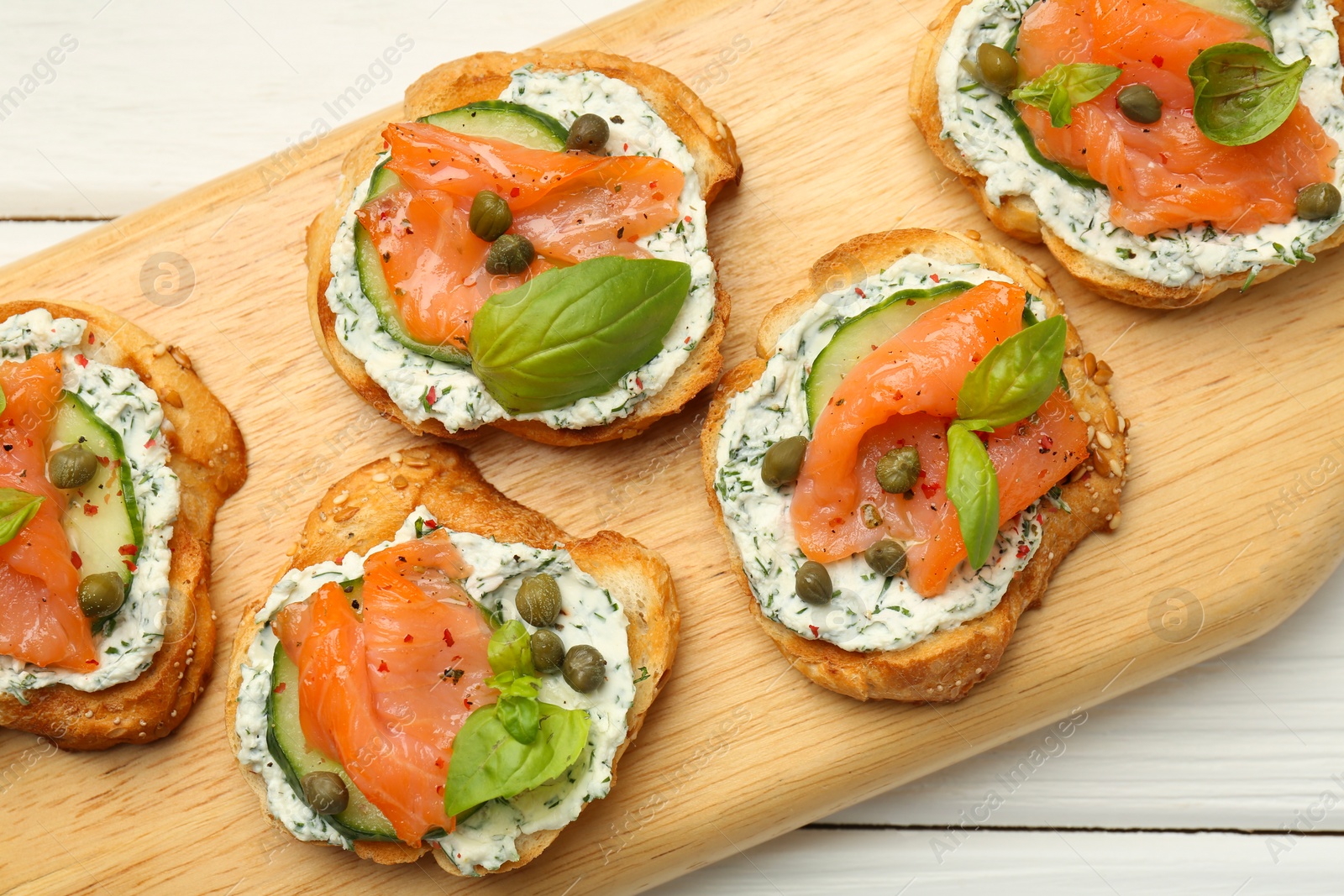 Photo of Tasty canapes with salmon, capers, cucumber and sauce on white wooden table, top view