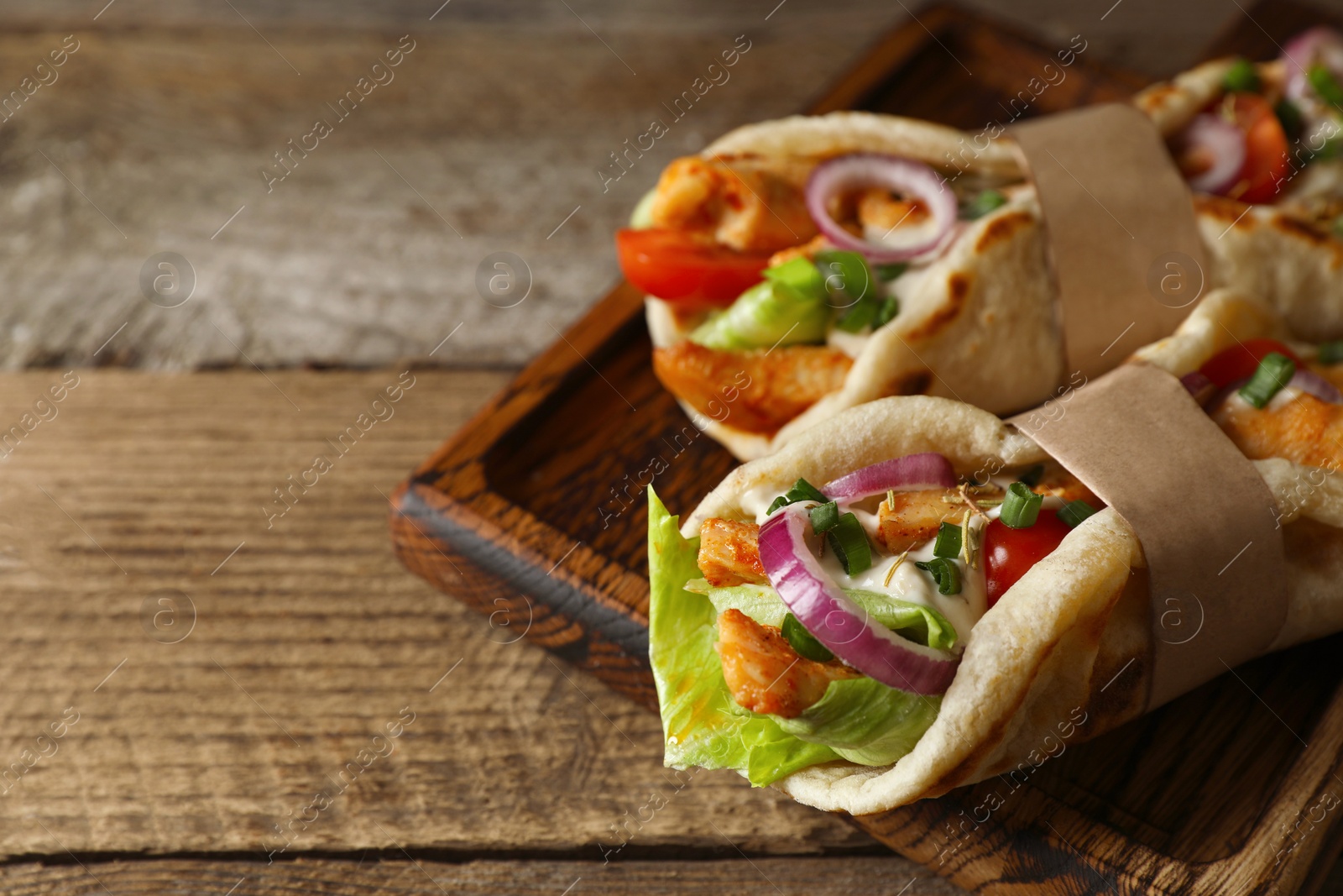 Photo of Delicious pita wrap with meat and vegetables on wooden table, closeup. Space for text