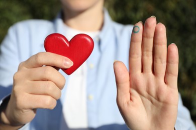 Photo of Woman showing blue circle as World Diabetes Day symbol and red heart outdoors, closeup