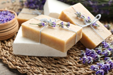 Photo of Handmade soap bars with lavender flowers on wicker mat, closeup