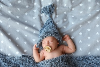 Cute newborn baby in warm hat sleeping on bed, top view