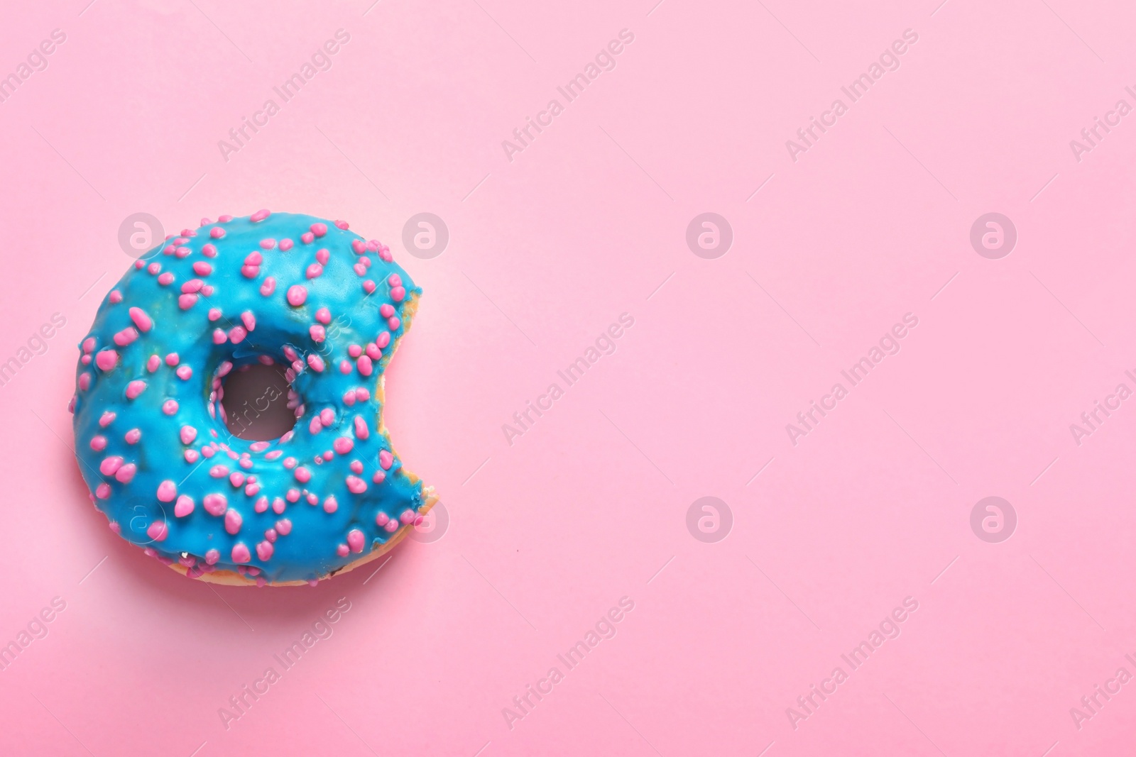 Photo of Delicious bitten doughnut with sprinkles on color background, top view