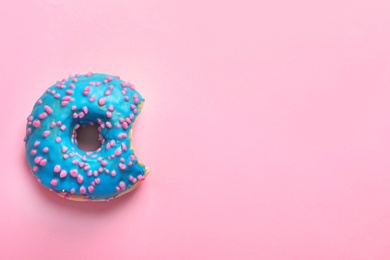 Delicious bitten doughnut with sprinkles on color background, top view