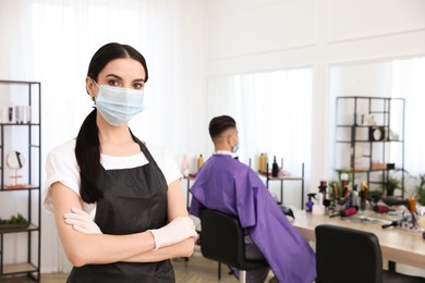 Professional stylist with protective mask in salon, space for text. Hairdressing services during Coronavirus quarantine