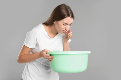 Photo of Woman with basin suffering from nausea on grey background. Food poisoning