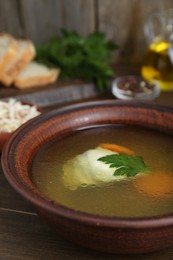Photo of Delicious chicken bouillon with carrot and parsley in bowl on wooden table, closeup