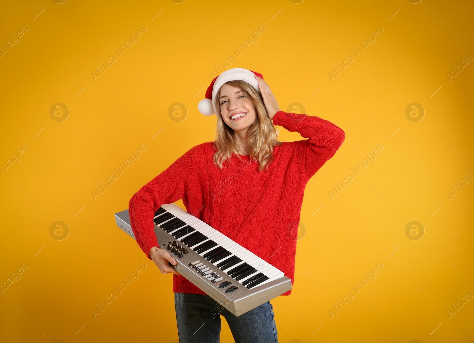 Photo of Young woman in Santa hat with synthesizer on yellow background. Christmas music