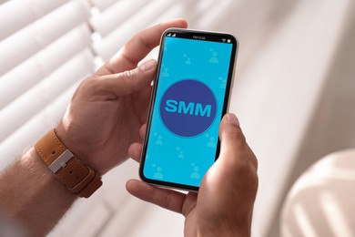 Image of SMM (Social Media Marketing) concept. Man using smartphone near window indoors, closeup