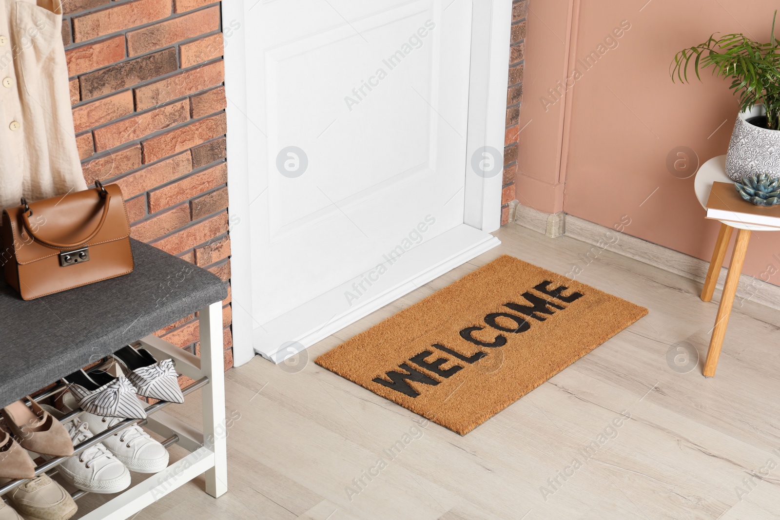Photo of Doormat with word Welcome near shoe rack on white wooden floor in hall