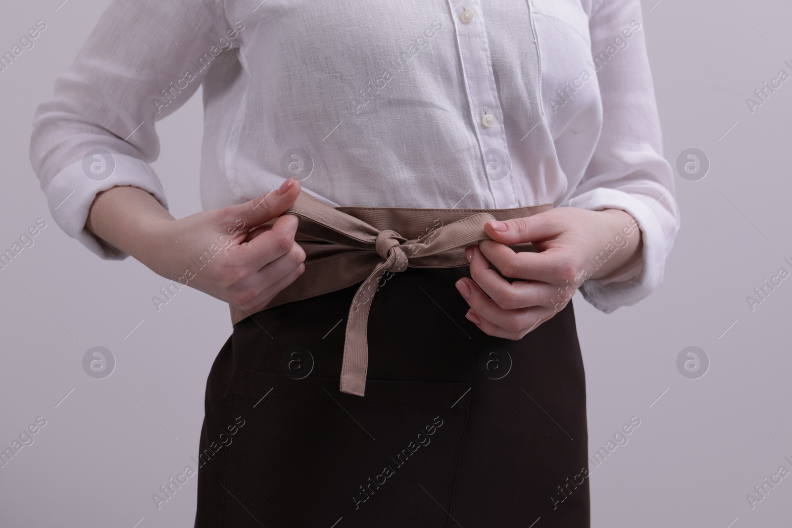 Photo of Woman putting on brown apron against white background, closeup