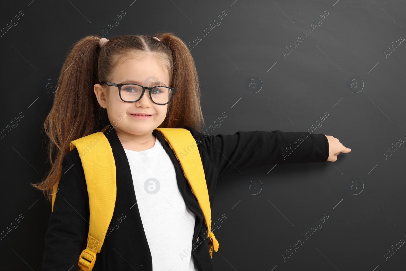 Photo of Happy little school child with backpack pointing at chalkboard