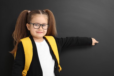 Photo of Happy little school child with backpack pointing at chalkboard