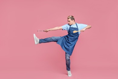 Portrait of confectioner holding spatula and whisk on pink background