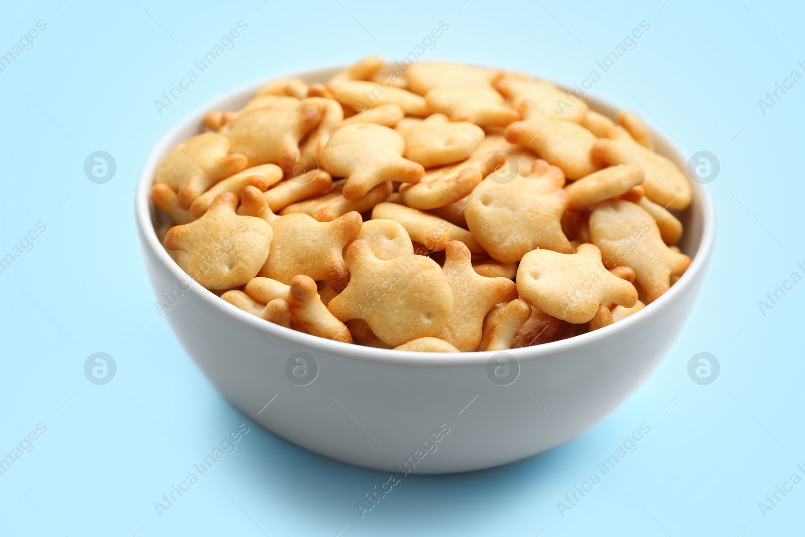 Photo of Delicious goldfish crackers in bowl on light blue background