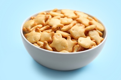 Photo of Delicious goldfish crackers in bowl on light blue background