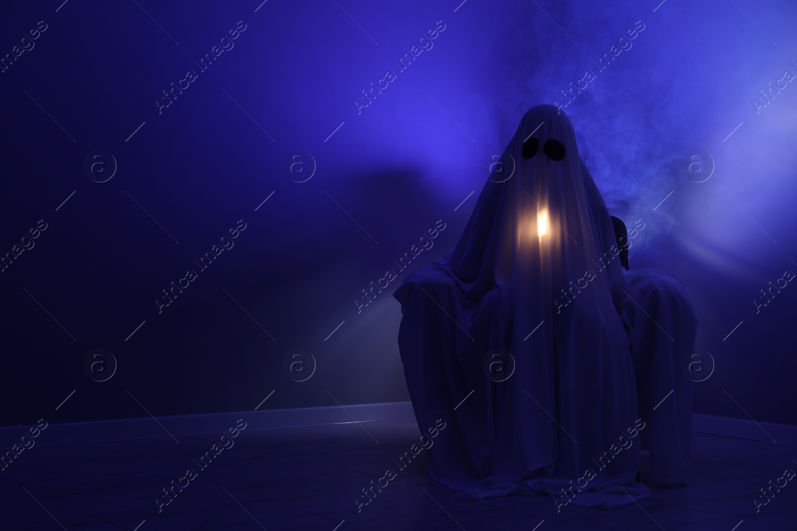 Photo of Creepy ghost. Woman covered with sheet sitting in armchair in blue light, space for text