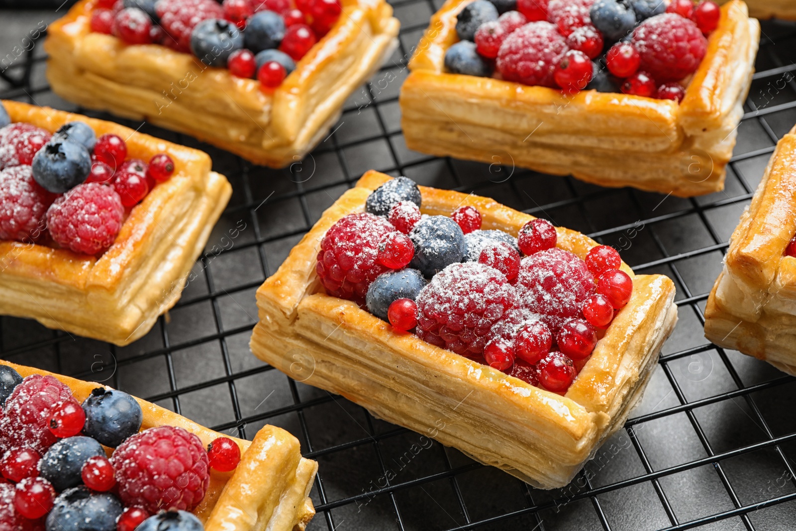 Photo of Cooling rack and fresh delicious puff pastry with sweet berries on grey table, closeup