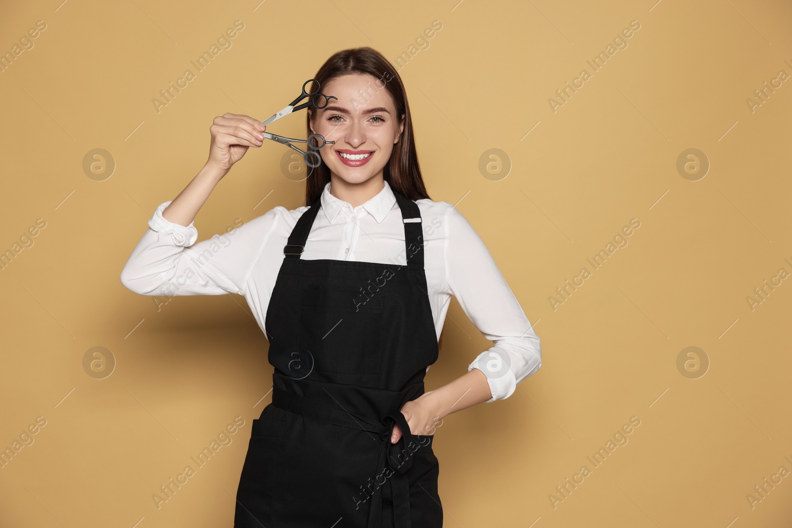 Photo of Portrait of happy hairdresser with professional scissors on beige background. Space for text