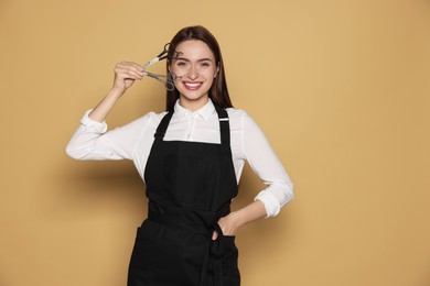 Portrait of happy hairdresser with professional scissors on beige background. Space for text