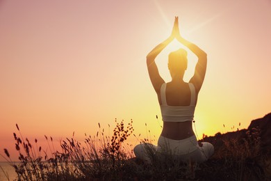 Image of Woman meditating outdoors at sunset, back view. Practicing yoga