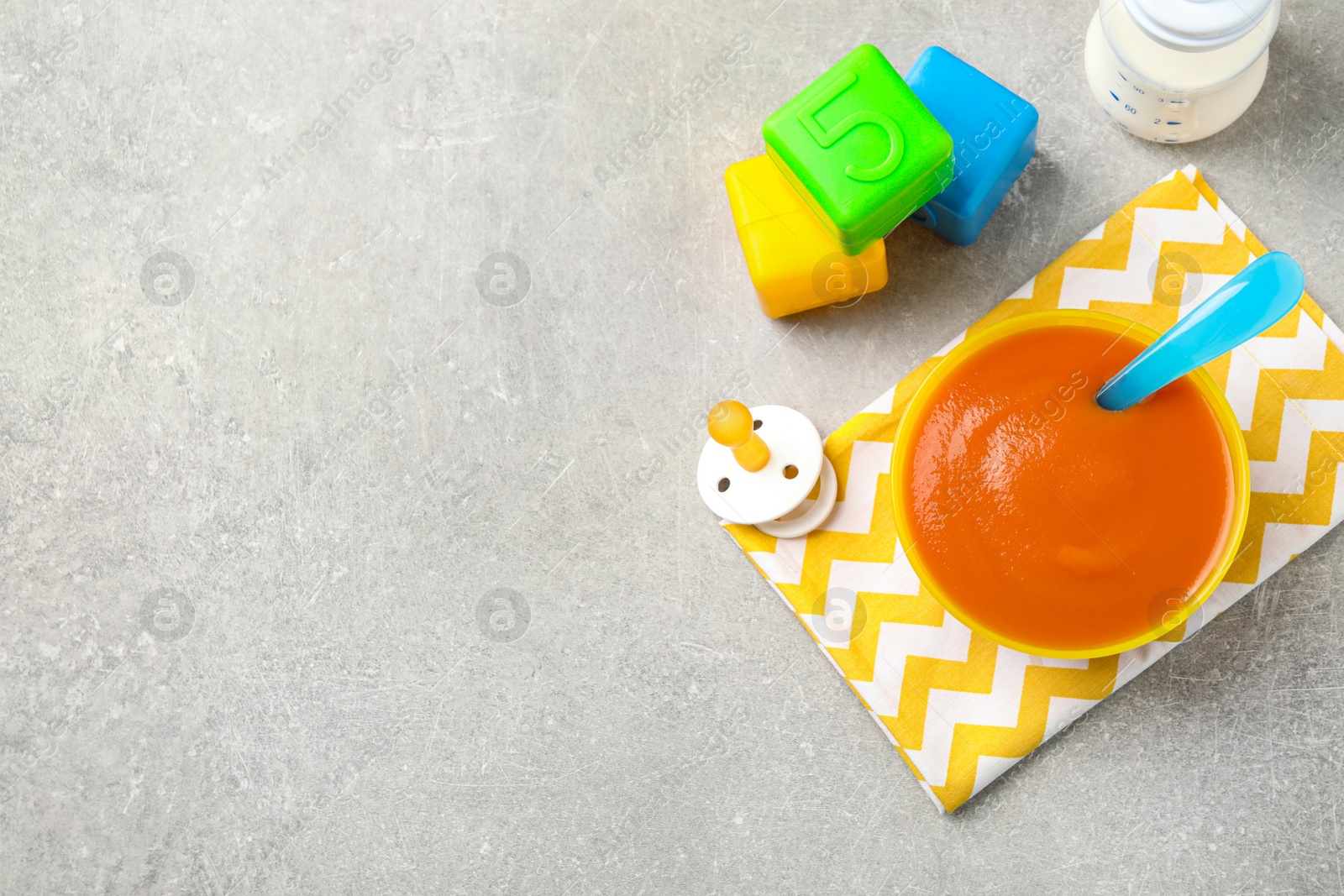 Photo of Flat lay composition with bowl of healthy baby food on grey table. Space for text