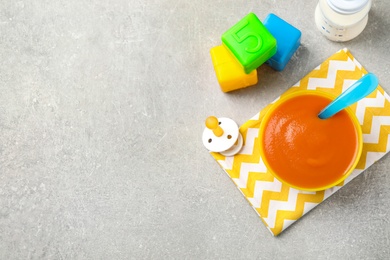 Photo of Flat lay composition with bowl of healthy baby food on grey table. Space for text