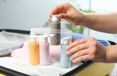 Photo of Woman with plastic bag of cosmetic travel kit packing suitcase, closeup