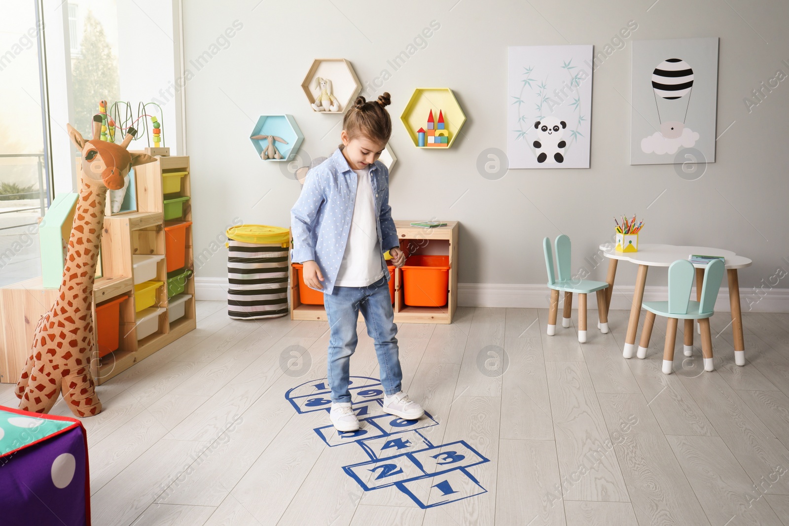 Photo of Cute little girl playing hopscotch at home