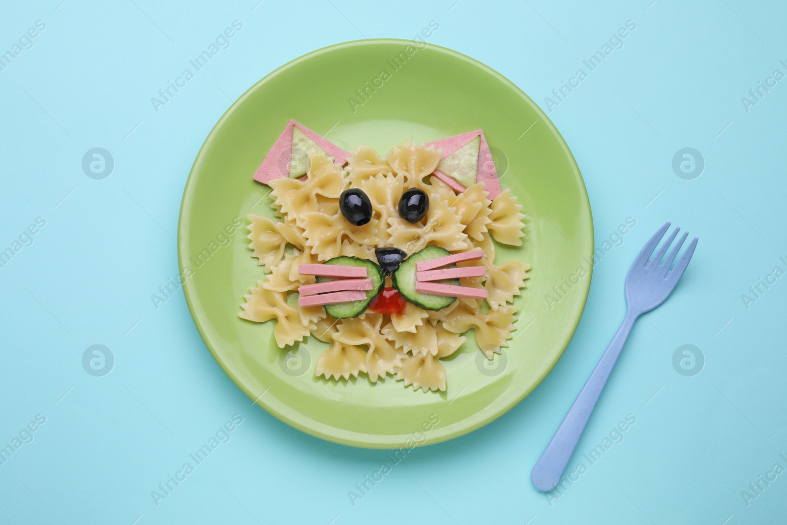 Photo of Creative serving for kids. Plate with cute cat made of tasty pasta, vegetables and sausage on light blue background, flat lay