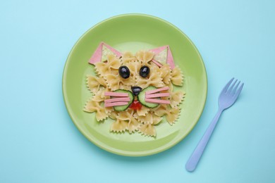 Creative serving for kids. Plate with cute cat made of tasty pasta, vegetables and sausage on light blue background, flat lay