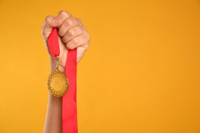 Woman holding gold medal on yellow background, closeup. Space for text
