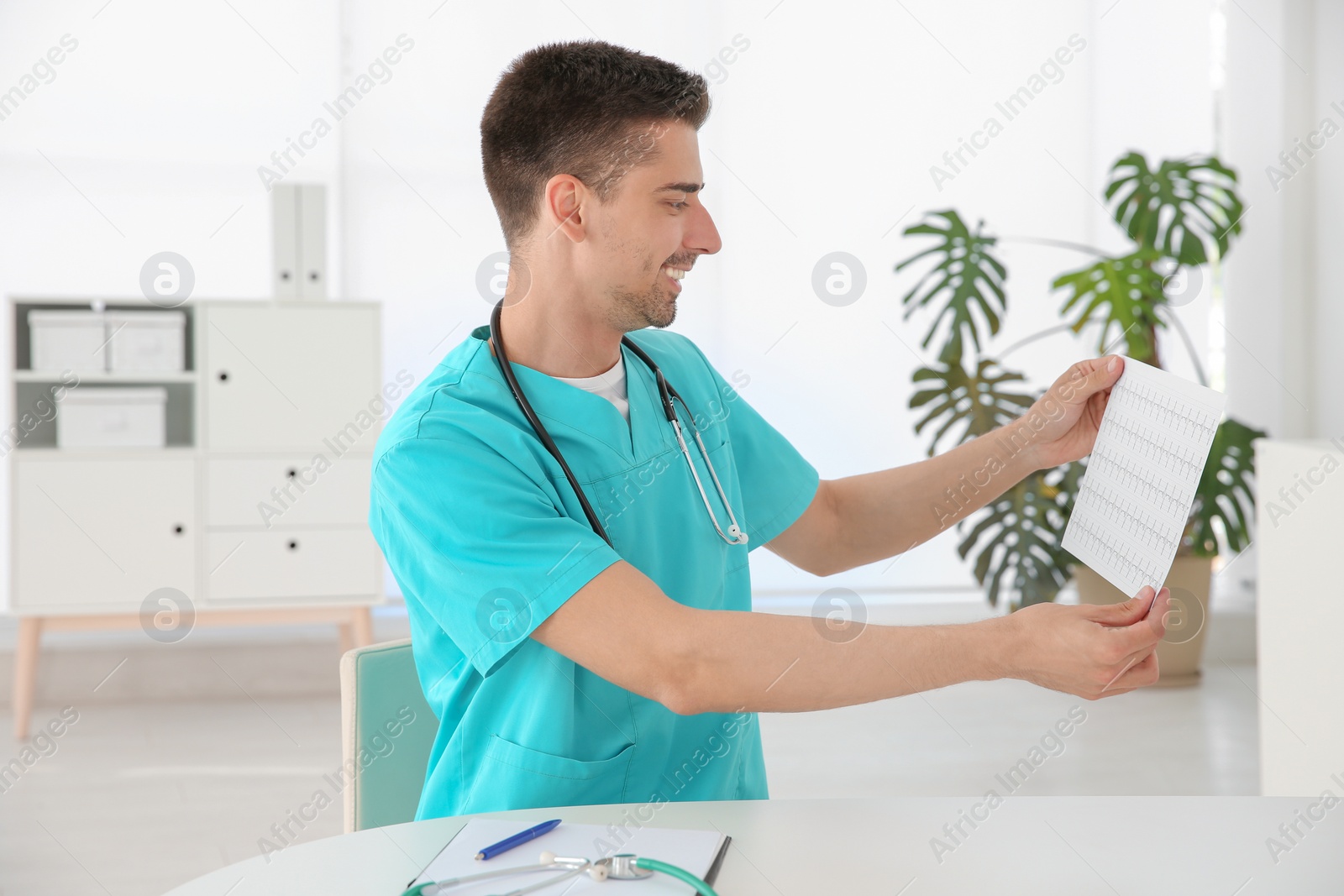 Photo of Young male doctor with cardiogram at workplace. Cardiology center