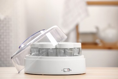 Modern yogurt maker with empty jars on table indoors