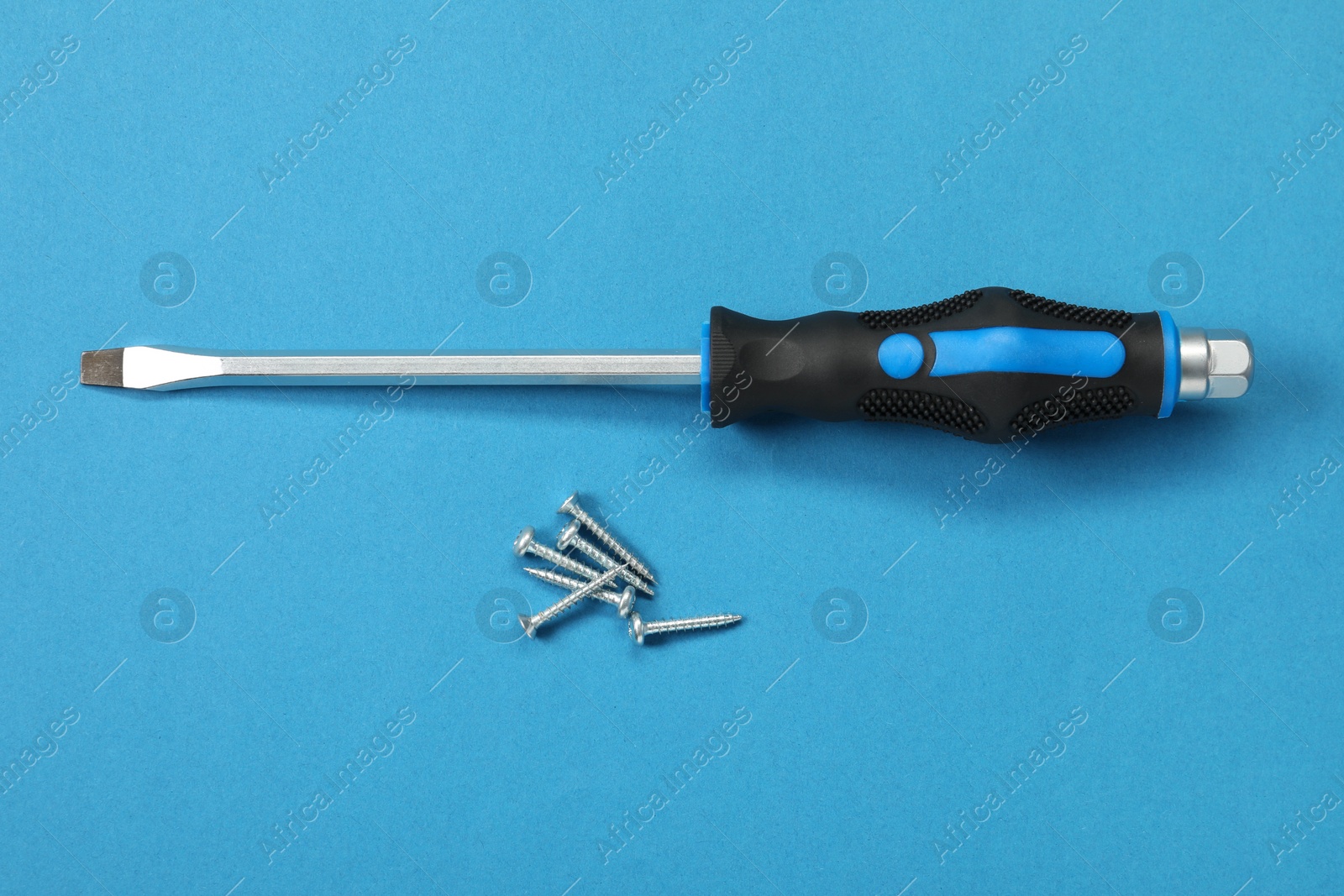 Photo of Screwdriver with black handle and screws on blue background, flat lay