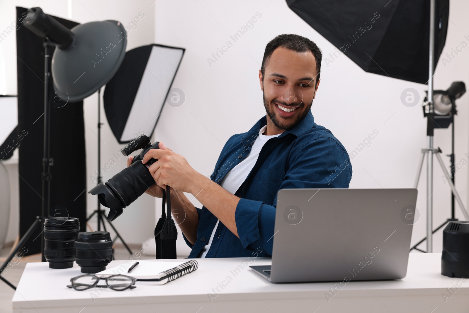 Photo of Young professional photographer with camera working on laptop in modern photo studio