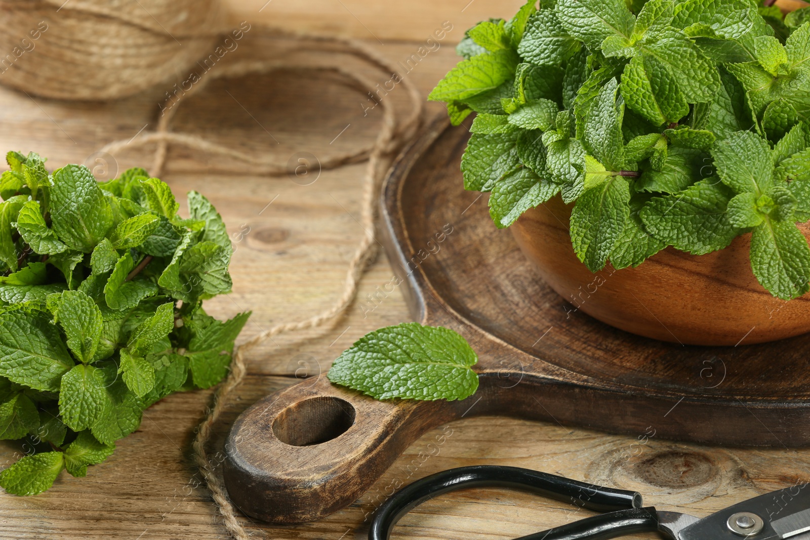 Photo of Bowl with fresh green mint leaves, twine and scissors on wooden table
