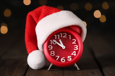 Alarm clock with decor on brown wooden table against blurred Christmas lights, closeup. New Year countdown