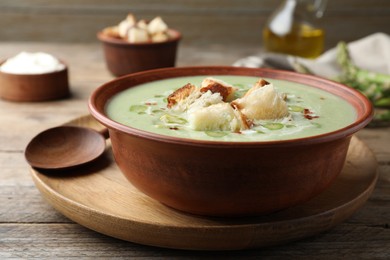 Photo of Delicious asparagus soup with croutons served on wooden table, closeup