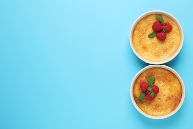 Delicious creme brulee with fresh raspberries in ramekins on light blue background, flat lay. Space for text