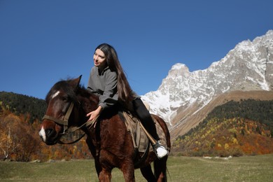 Photo of Young woman riding horse in mountains on sunny day. Beautiful pet